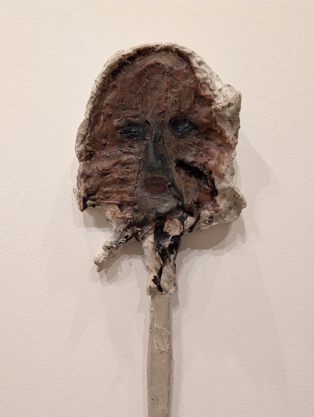 Abstract art piece resembling a face made of meat on a popsicle stick.