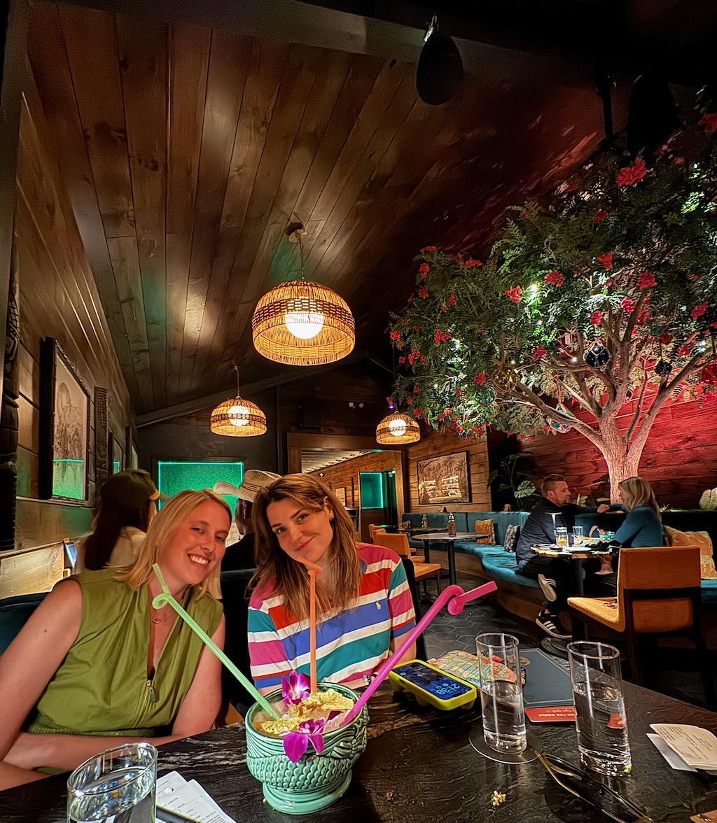 Two people seated at an indoor tiki bar booth with a punch bowl.
